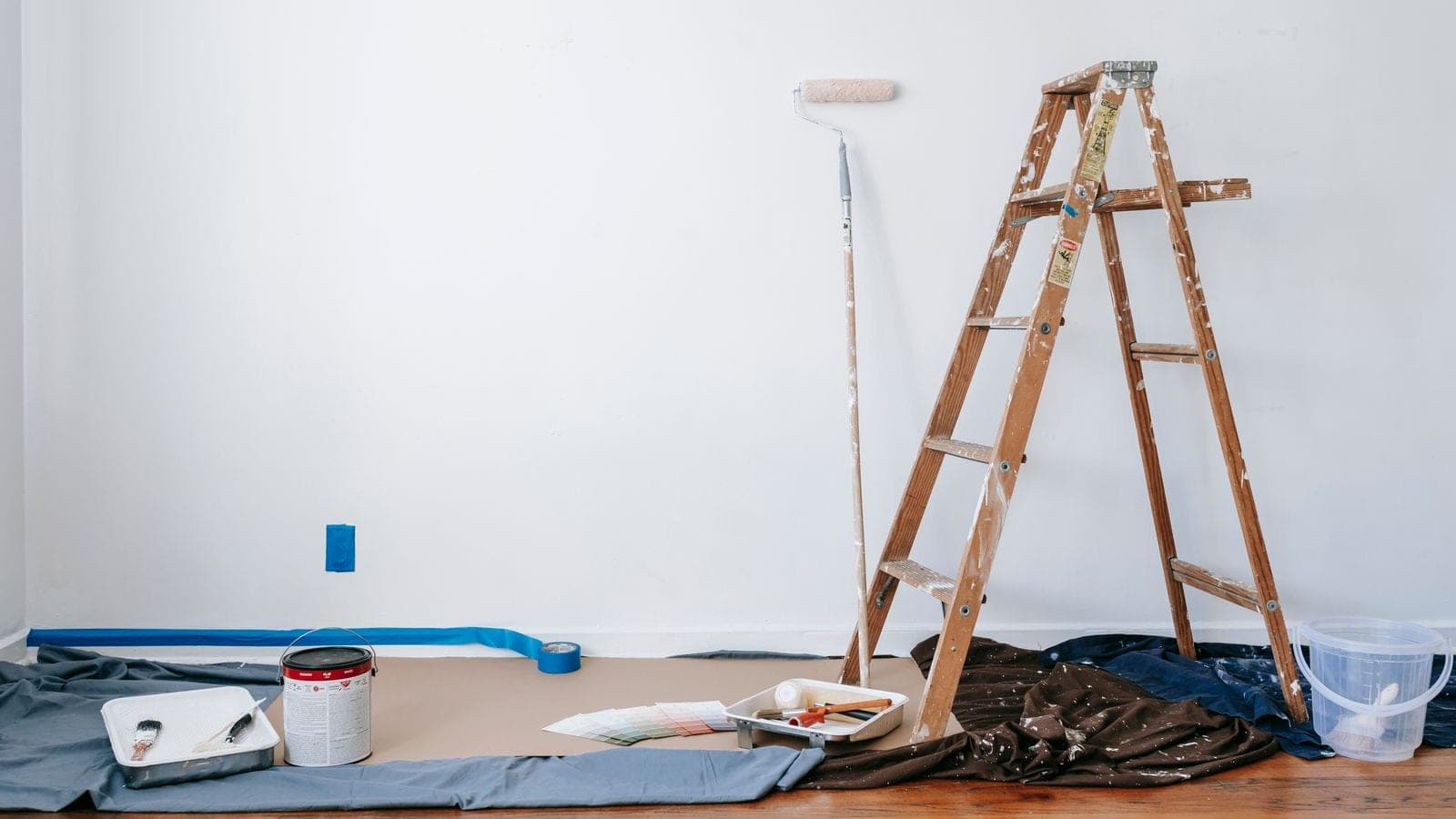 Trapladder, verfroller en afdekzeilen in een kamer die klaargezet is voor binnenschilderwerk
