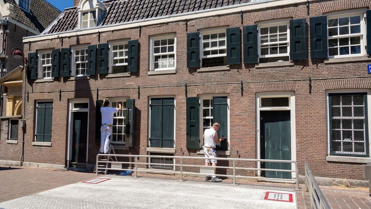 Twee schilders werken aan de kozijnen en luiken van een Nederlands pand met bakstenen gevel